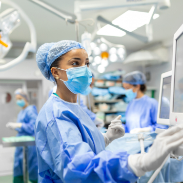 Anesthetist Working In Operating Theatre Wearing Protecive Gear checking monitors while sedating patient before surgical procedure in hospital